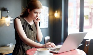 Salesforce: Woman in coffee shop on mobile and using laptop.